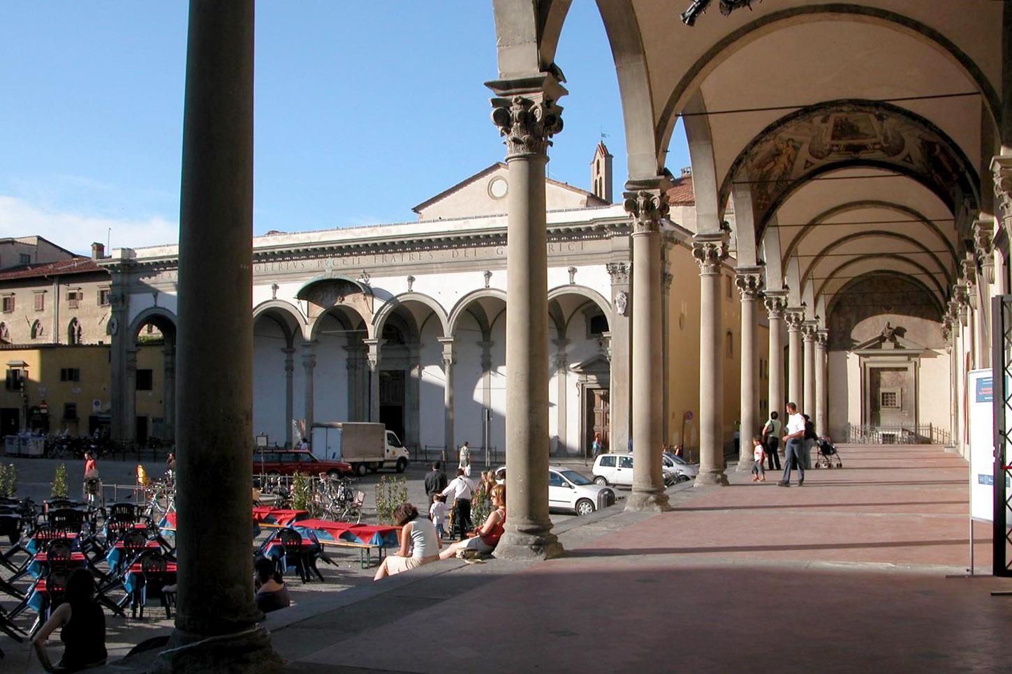 Piazza in Italy, with an arched walkway on the right and people sitting in the open area on the left.