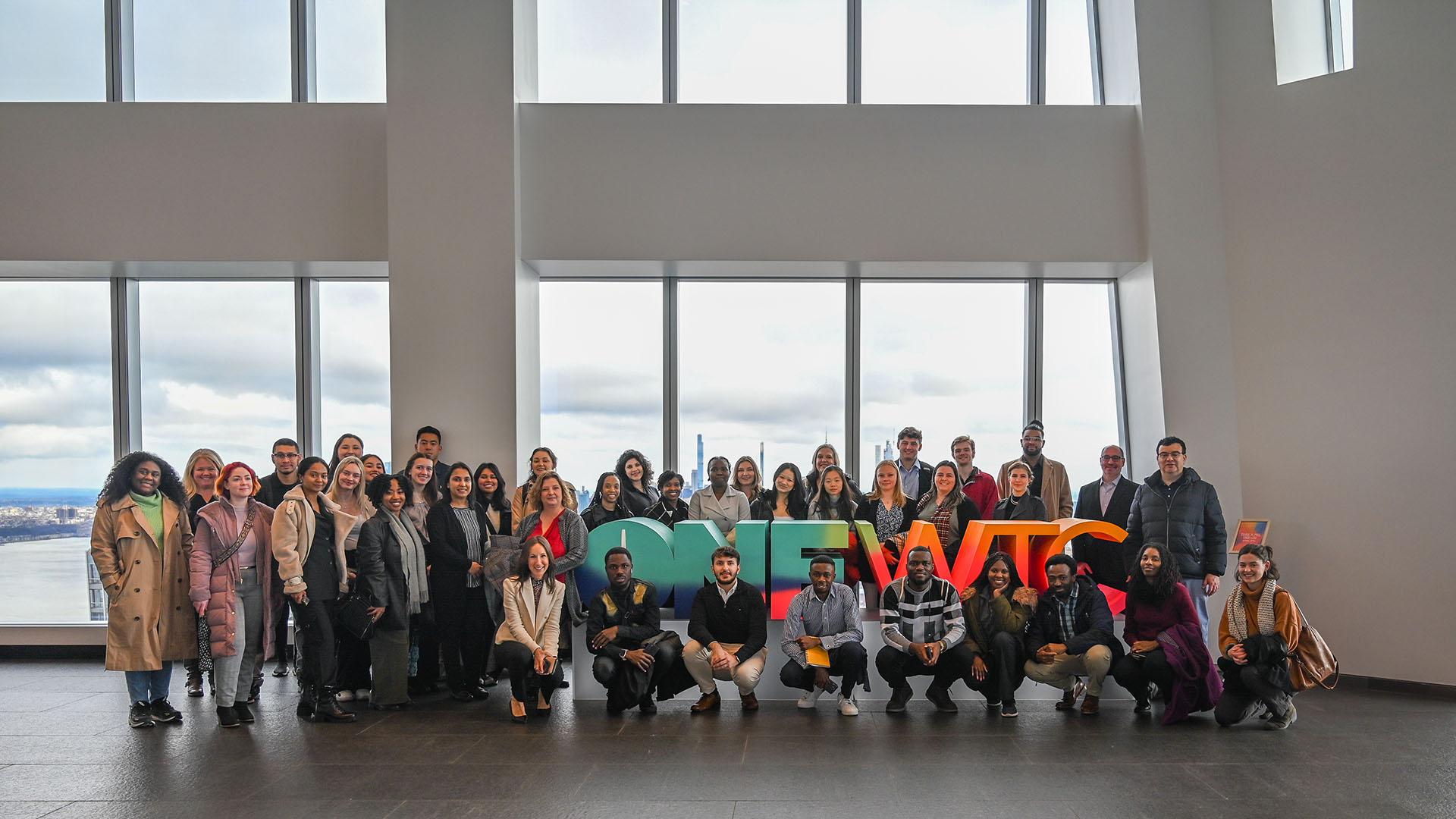 Large group of students posing together in a white building with colorful signage