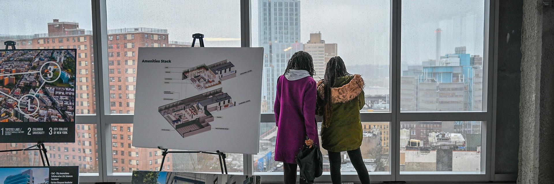 Two women looking out of a skyscraper there are poster boards to the left of them