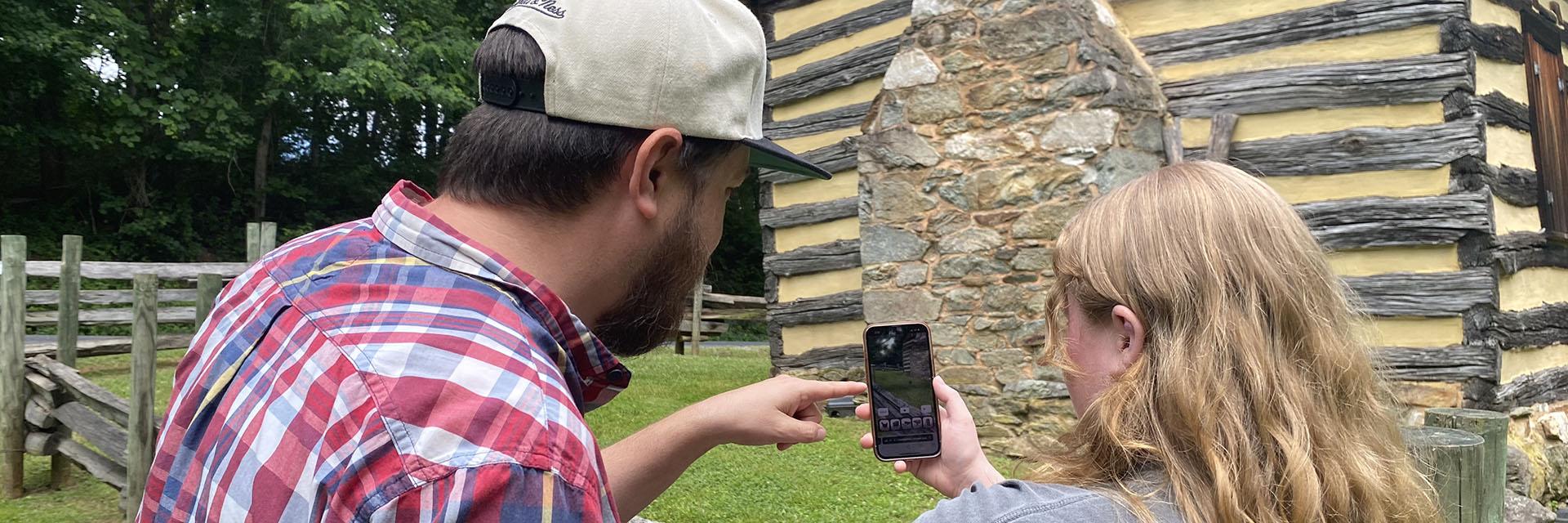 A professor and student looking at an Augmented Reality app with Oakley Cabin in the background.