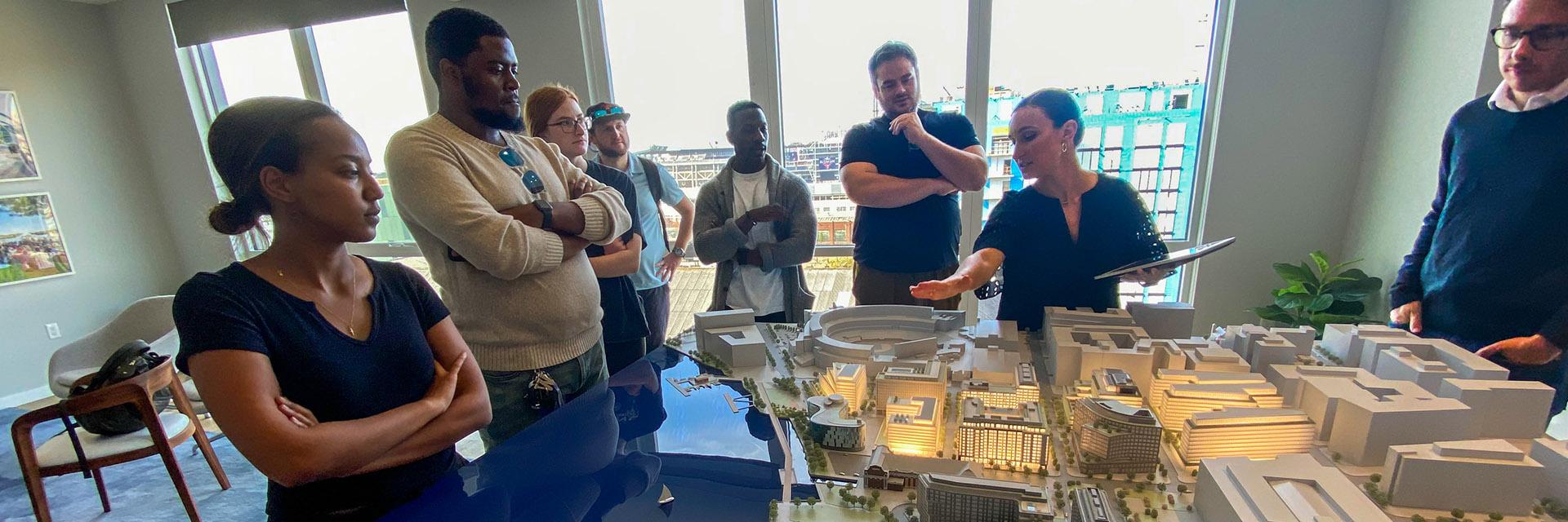 Students surrounded by a large model of Navy Yard, a woman gesturing and talking
