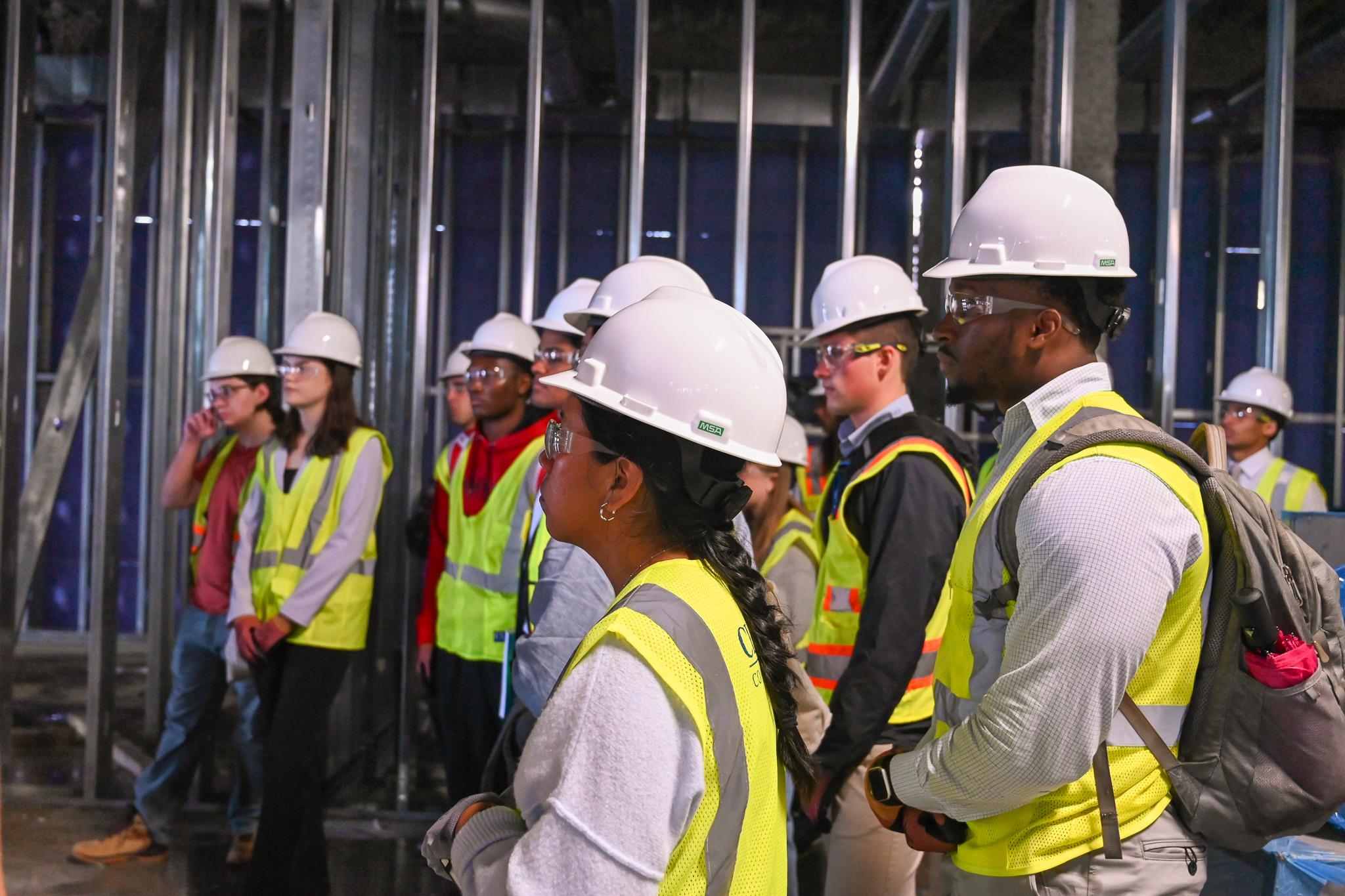 Students wearing construction hats and vests at a site