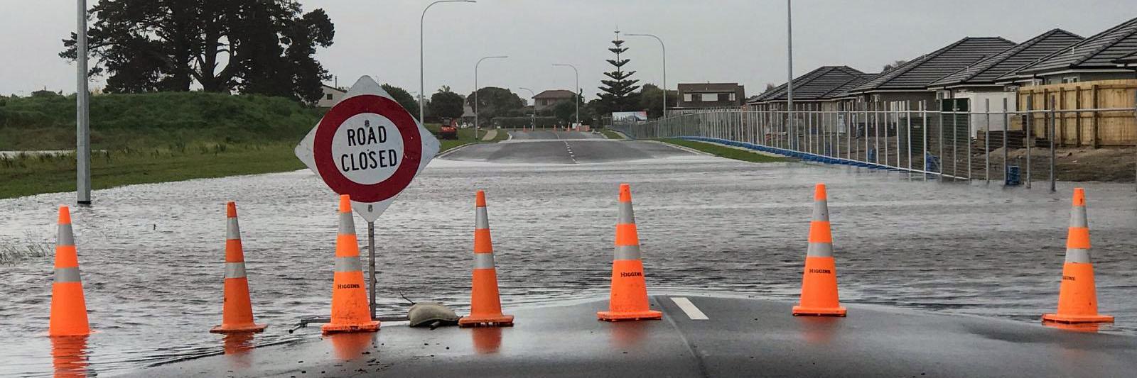 A flooded road with a "road closed" sign and orange warning traffic cones