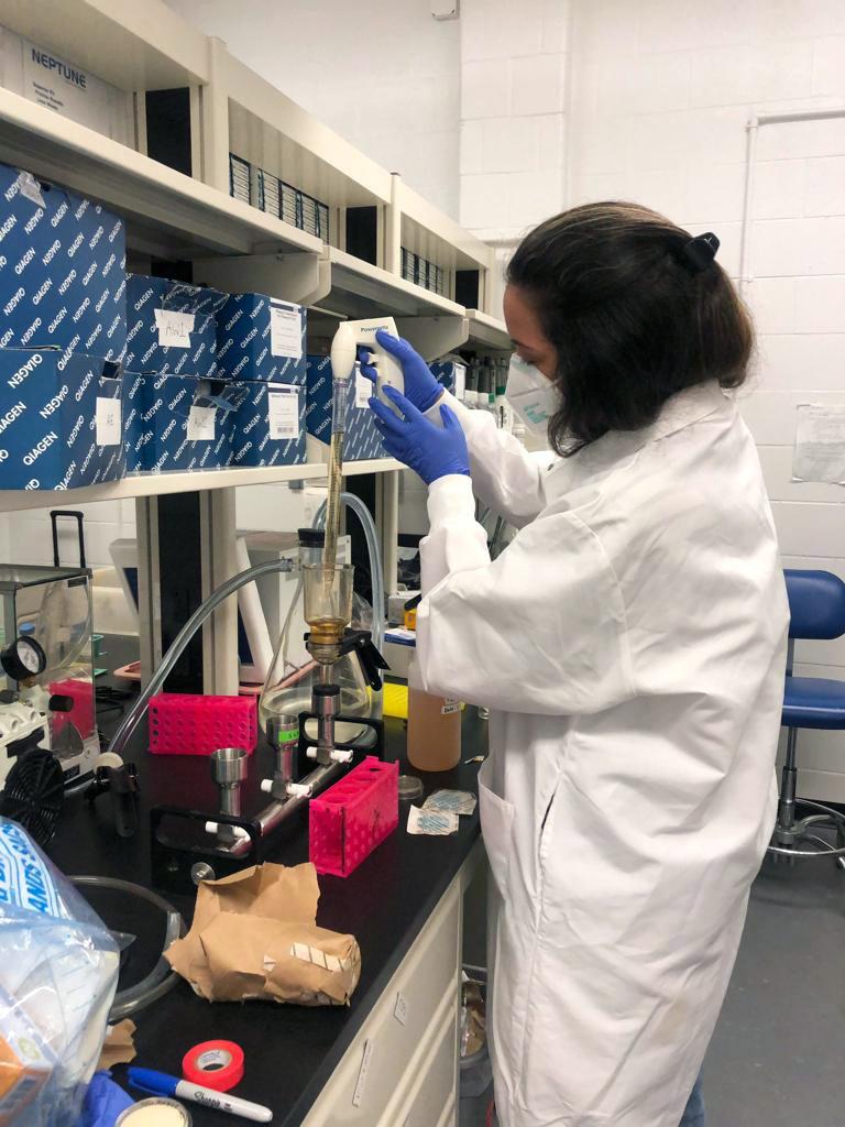 Woman testing water in a lab, dressed in a lab coat, gloves and masks