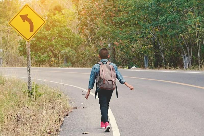 Child walking to school on the side of the road