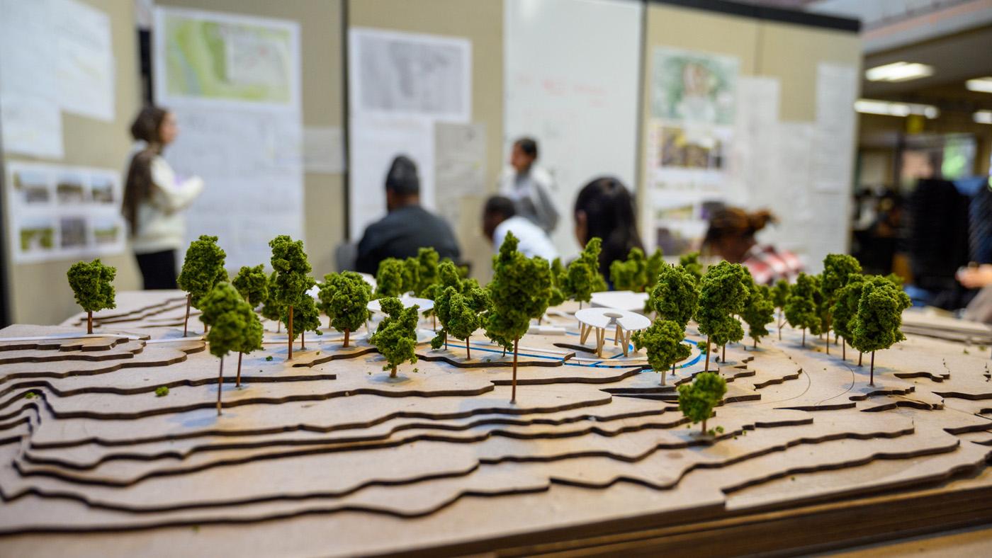 Architecture model in foreground with students presenting in the back background