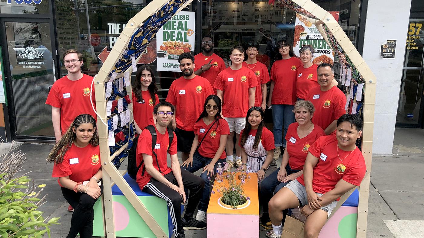 Group shot of students, faculty and staff in red t-shirts sitting within a wooden structure