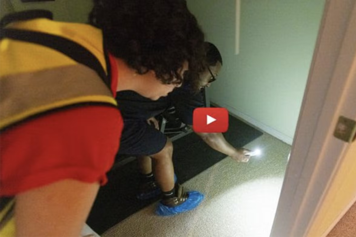 Two people looking under a wall with a flashlight for sewage backup