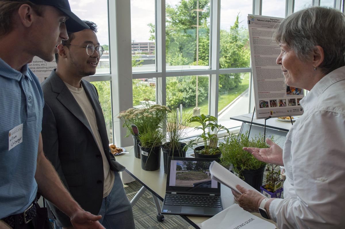 Students and attendee by plants in containers and a laptop for their project showcase