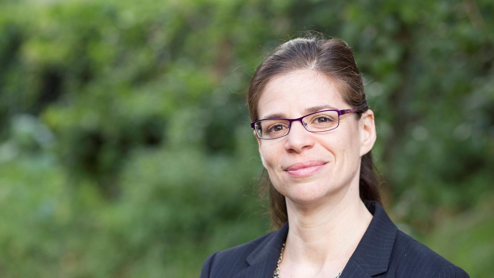 Woman in glasses smiling for photograph behind greenery 