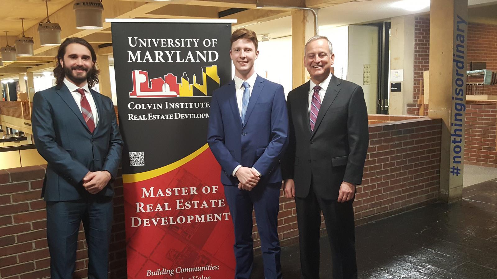 A group of three men in business attire smiling for a photograph with a banner saying "Master of Real Estate Development" between them. 