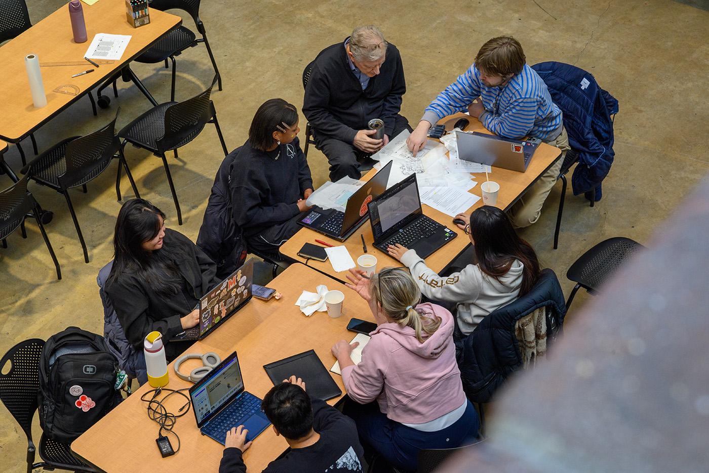 Students working on a hackathon at a table surrounded by laptops and paper
