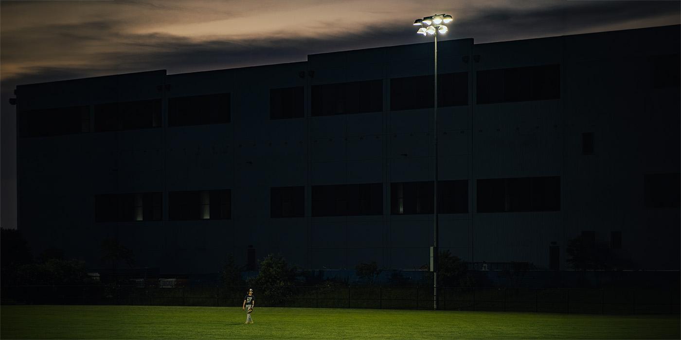 Boy playing baseball under the lights with a data center behind the fence