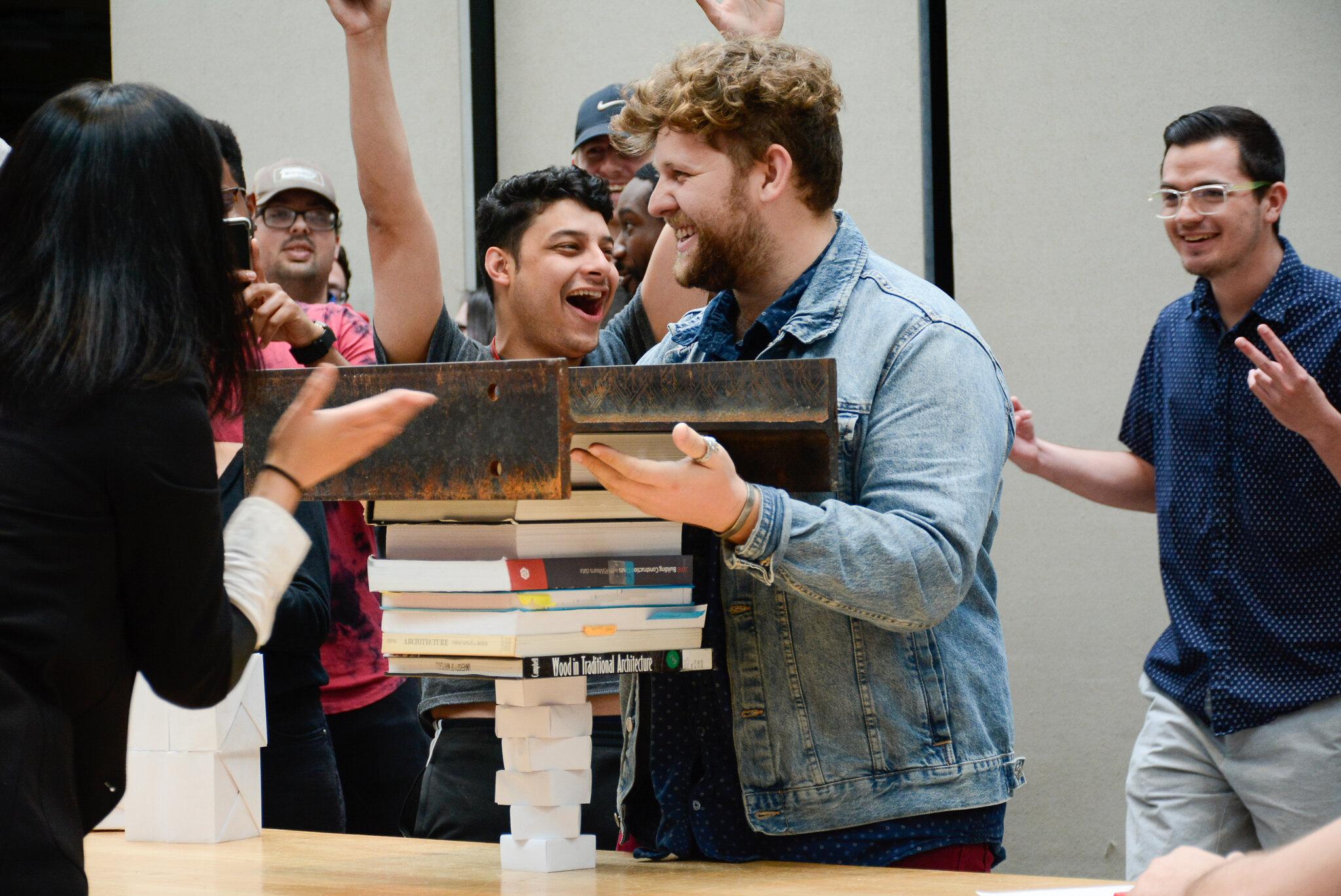 Students celebrating as their origami structure withholds lots of weight from books and a steal structure