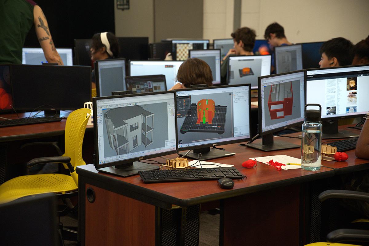 Computers showing architecture models and students working in the background