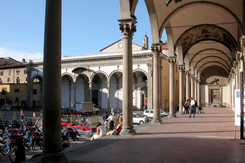 Piazza in Italy, with an arched walkway on the right and people sitting in the open area on the left.