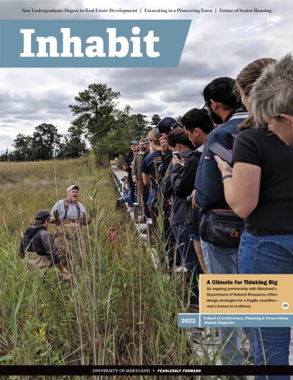 Inhabit Magazine cover of people lined up on a small bridge looking down at a man speaking in tall grass